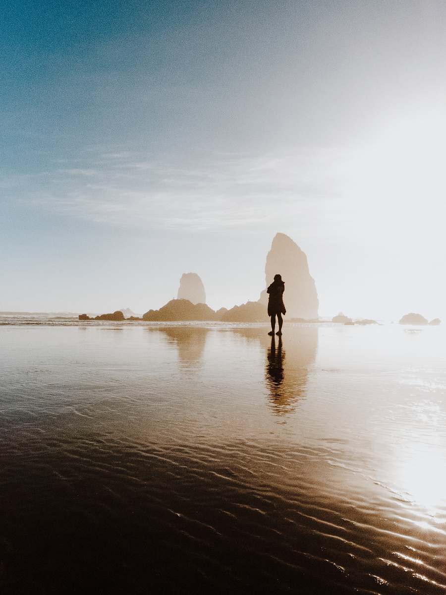 haystack rock person standing in shallow body of water near boulders united states
